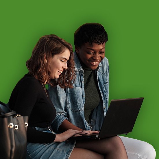 Two women sitting together using a laptop against a green background